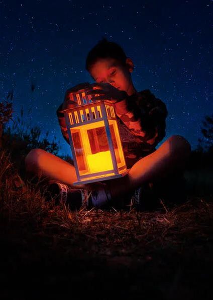 boy sits under the stars looking at candle lantern
